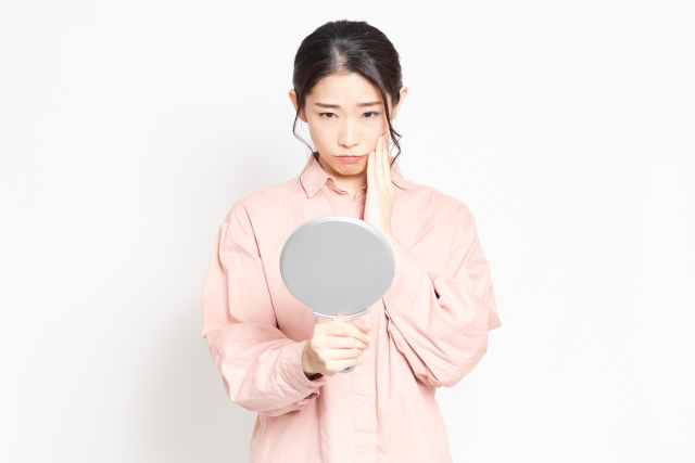 鏡を見て顔のたるみに悩んでいる女性