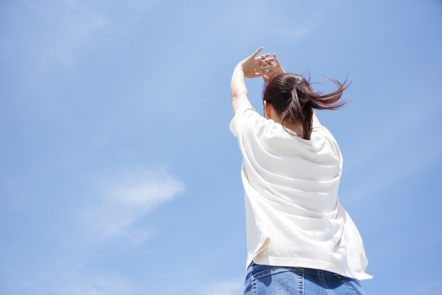 青空に向かって伸びをする女性