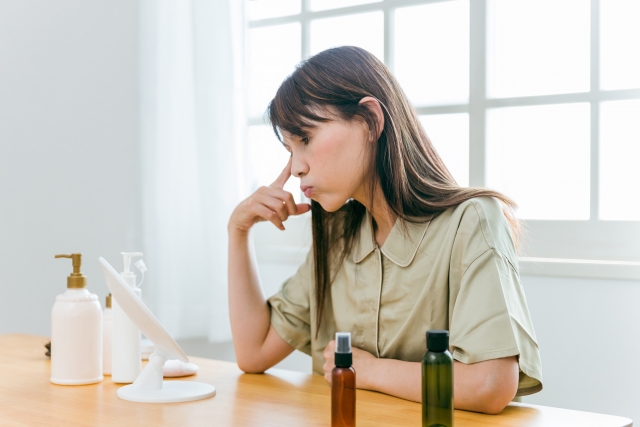 顔を鏡で見ながら悩んでいる女性