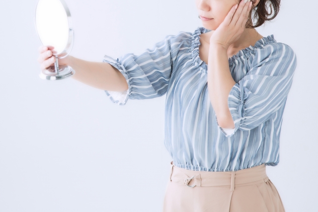 顔を鏡で見ながら悩んでいる女性