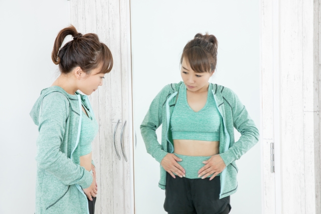 お腹を内側と外側から温めることで、どのような効果が出たかを鏡で確認する女性