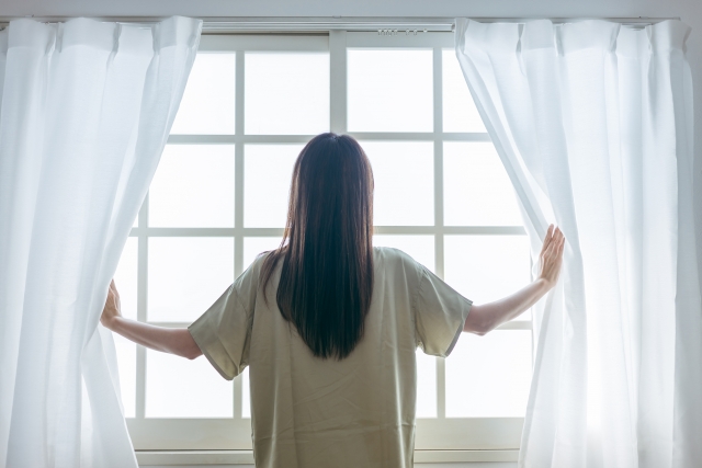 起床してすぐカーテンを開け、太陽の光を浴びて体内時計をリセットする女性
